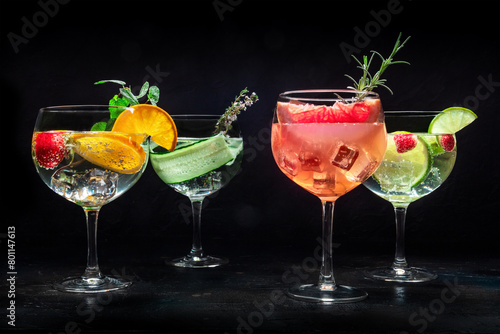 Fancy cocktails with fresh fruit. Many gin and tonic drinks with ice at a party, on a black background. Alcohol with herbs and flowers