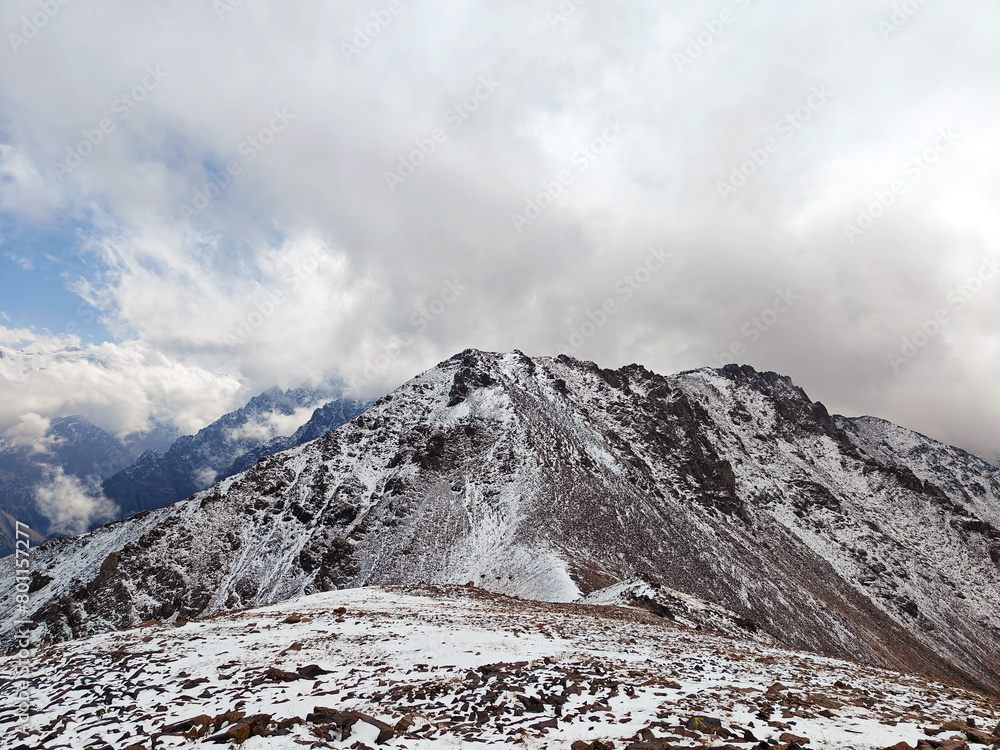 Snow-dusted mountain ridge with rugged terrain under a cloudy sky