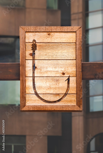 A large fishing hook is depicted on a wooden plank