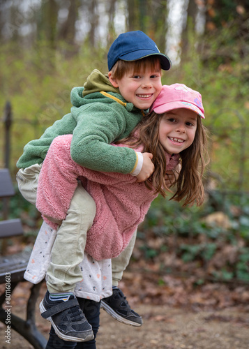 Cute brother and sister frolicking outdoors. A girl holds a boy on her back. Fun games in nature. Joyful and happy childhood