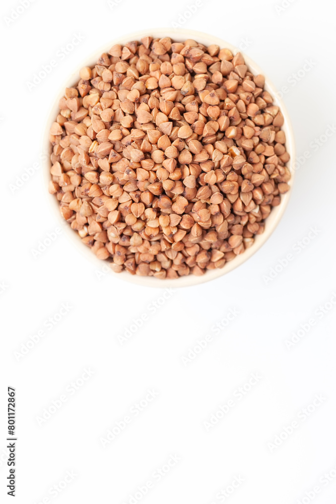 Uncooked, brown buckwheat grains in bowl on white background. Top view. Space for a text Uncooked, brown buckwheat grains in bowl on white background. Top view. Space for a text
