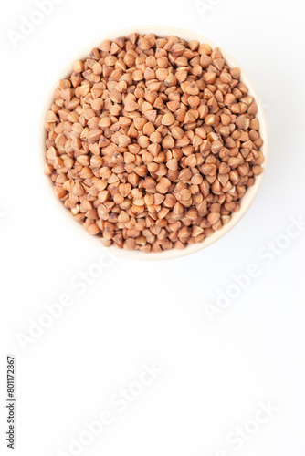 Uncooked, brown buckwheat grains in bowl on white background. Top view. Space for a text