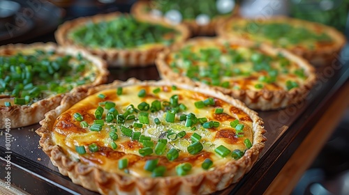  A tight shot of multiple pies with green onions atop a black tray, situated on a table
