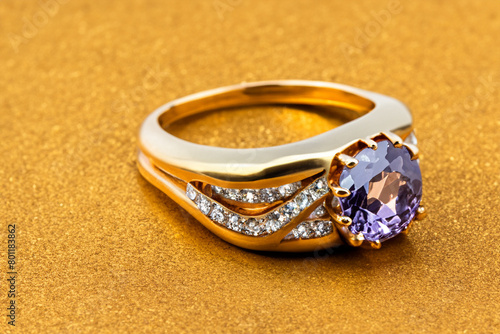 Golden ring. a beautiful shiny gold ring with a purple stone lies on a yellow table, close-up top view, costume jewelry concept