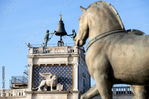 View of Clock Tower with the Horses of Saint Mark defocused in foreground. Winged Lion and The Moors striking the bell statues on a beautiful sunny day in Venice; Italy