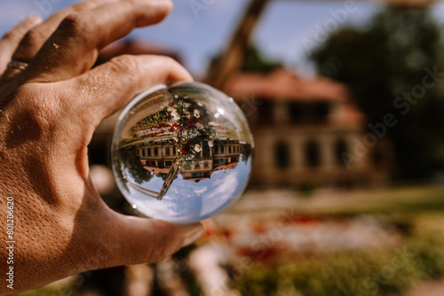 Valmiera, Latvia - August 19, 2023 - A crystal ball in a hand vividly reflects and inverts a historic building, surrounded by a lush garden and clear blue sky. photo