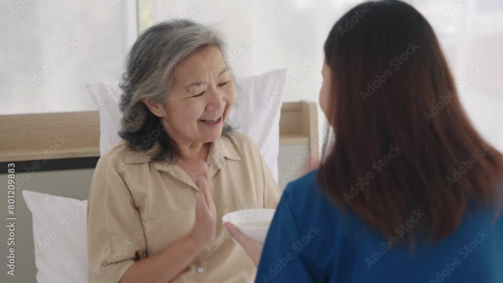 Handheld medium shot, Selective focus, Face of aged woman smile during Asian young caregiver female help with feeding breakfast to her on bed, They are smile and talking with happy together Handheld medium shot, Selective focus, Face of aged woman smile during Asian young caregiver female help with feeding breakfast to her on bed, They are smile and talking with happy together