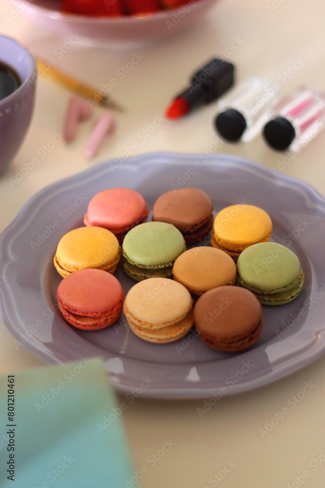 Plate of pastel macarons, cookies and chocolate, cup of tea of coffee, glass of bubble water, various berries, books and accessories on the table. Selective focus, pastel colors. Plate of pastel macarons, cookies and chocolate, cup of tea of coffee, glass of bubble water, various berries, books and accessories on the table. Selective focus, pastel colors.