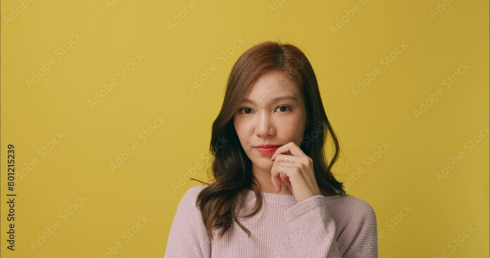 Happy young Asian woman thinking about something. Isolated on yellow background in studio. Happy young Asian woman thinking about something. Isolated on yellow background in studio.