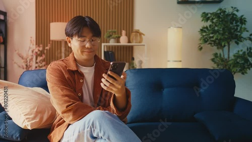 Asian man in glasses shopping online on cellphone, adding an item into a cart