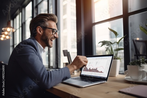 Joyful man in smart casual outfit using laptop, displaying graphs, laughing in modern office with daylight and plants. Ideal for themes of success, business analytics, and workplace enthusiasm