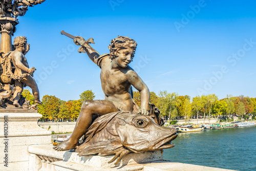 Bronze statue of a genius on a fish and holding a trident spear of Pont Alexandre III bridge in Paris, France