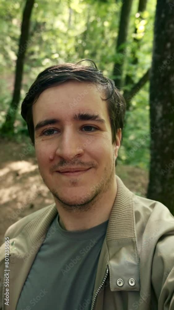 A man captures a self-portrait photograph in a wooded area. Vertical footage. A man captures a self-portrait photograph in a wooded area. Vertical footage.