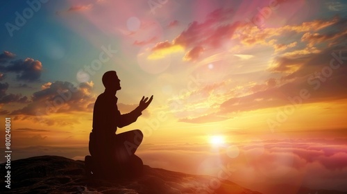 Silhouette of a person kneeling with his arms open and looking at the sky at sunset