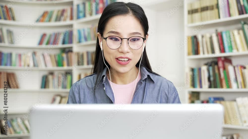Smiling asian female student talking on video call using laptop computer sitting at university library. Happy positive young woman in glasses and headphones having conversation with friend. Close up Smiling asian female student talking on video call using laptop computer sitting at university library. Happy positive young woman in glasses and headphones having conversation with friend. Close up