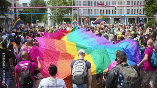 Many people wave huge rainbow flag. Big crowd walk city street. Fun lgbt community symbol. Stop no homophobia concept. Joy pride month fest. Bi gay men go csd love day party. Queer culture festival. photo