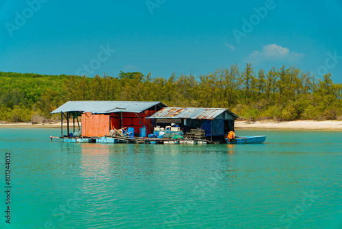 Small floating houses between the horizon line that separates the sea from the sky and set against a backdrop of plains and mountains. Floating houses used by fishermen as a place to cultivate fish