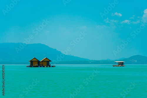 Small floating houses between the horizon line that separates the sea from the sky and set against a backdrop of plains and mountains. Floating houses used by fishermen as a place to cultivate fish