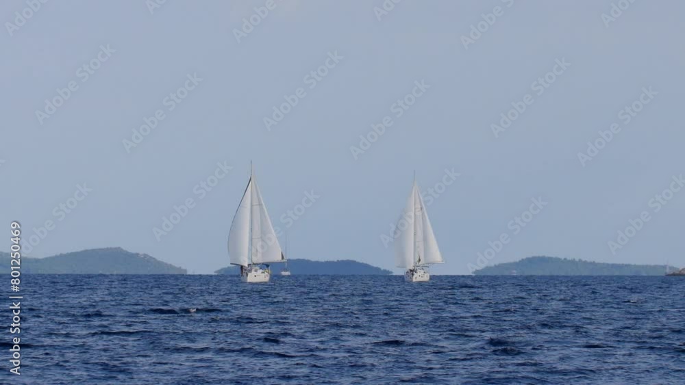 Two sailboats are sailing in the ocean. The sky is clear and the water is calm. The boats are white and are sailing in opposite directions Two sailboats are sailing in the ocean. The sky is clear and the water is calm. The boats are white and are sailing in opposite directions