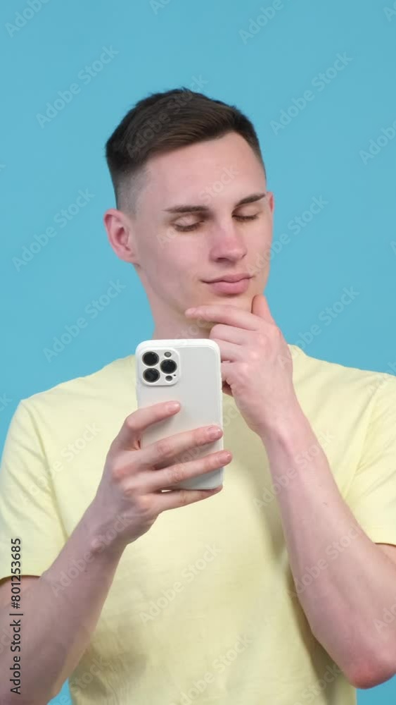Thoughtful Caucasian man using smartphone for messaging online on blue background. Internet relaxation and leisure concept. Vertical video. Thoughtful Caucasian man using smartphone for messaging online on blue background. Internet relaxation and leisure concept. Vertical video.