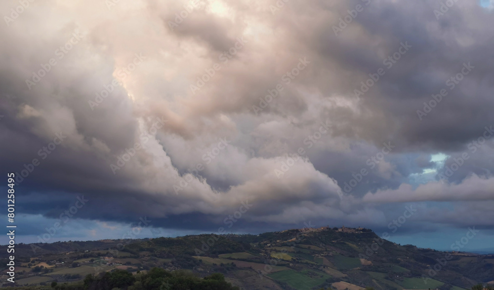 Fototapeta premium Enorme nuvola bianca sopra il paese in cima alla collina porta la pioggia in una giornata di sole invernale