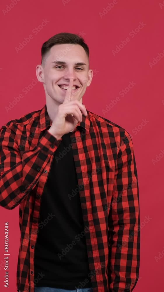 Joyful and excited man showing hush gesture with finger on lips on red background. Gossip, mystery, conspiracy concept. Vertical video. Joyful and excited man showing hush gesture with finger on lips on red background. Gossip, mystery, conspiracy concept. Vertical video.