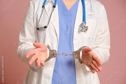 Female doctor with hands handcuffed during arrest, studio pink background. Nurse in uniform with stethoscope on red studio background © Андрей Журавлев