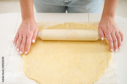 Closeup on female hands rolling dough with rolling pin on white background. Process of cooking pecan pie in home kitchen for American Thanksgiving Day. © Андрей Журавлев