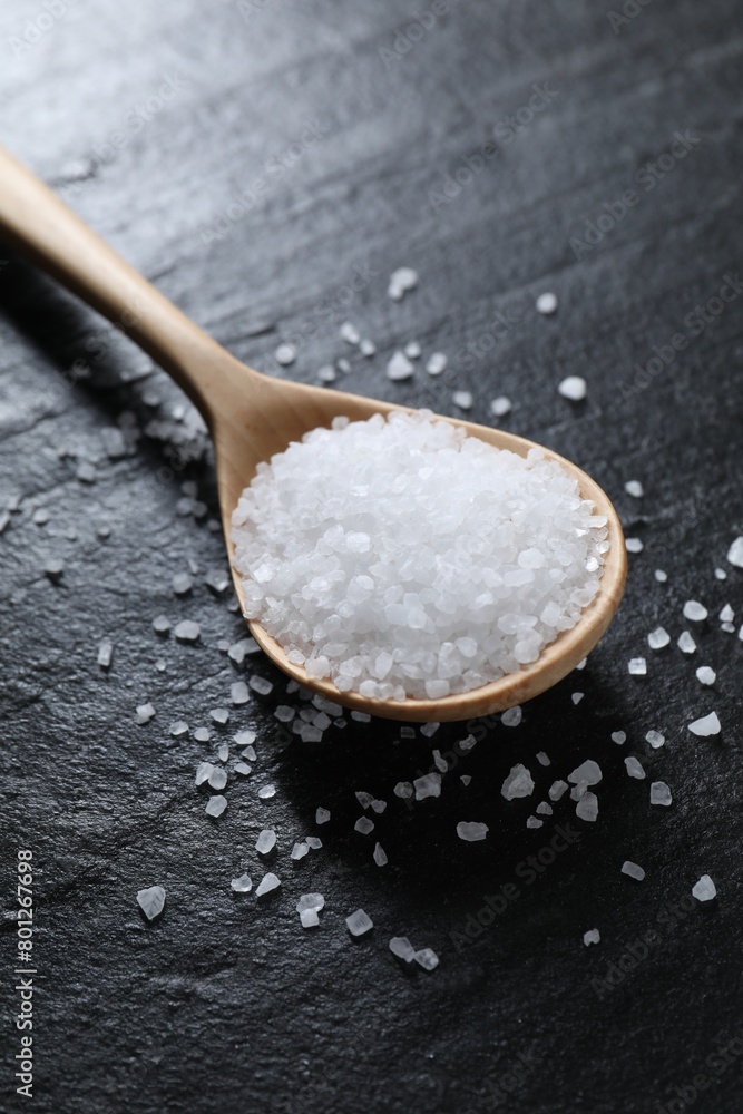 Organic white salt and spoon on black table, closeup Organic white salt and spoon on black table, closeup