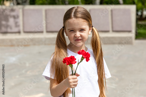 Victory Day concept. Little girl with two red carnations at the Eternal flame near the monument of Unknown soldiers tomb. 9 May celebration