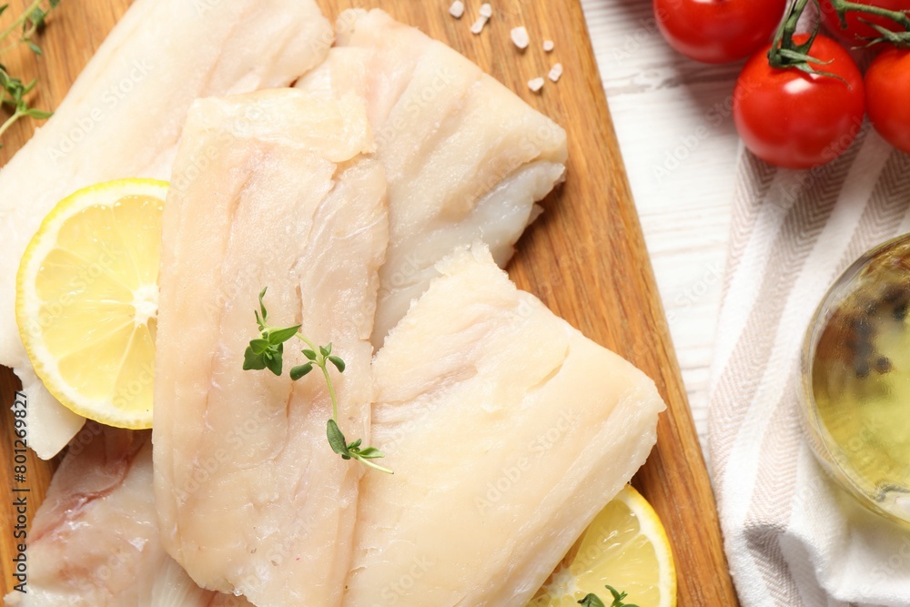Pieces of raw cod fish, lemon and tomatoes on white wooden table, top view Pieces of raw cod fish, lemon and tomatoes on white wooden table, top view