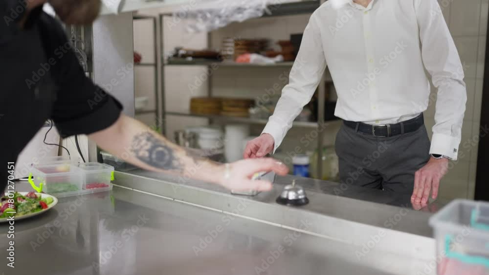 A male chef in a black uniform passes the finished dish to the waiter for packaging and delivery of the order outside the restaurant. Packaging a restaurant dish for home delivery A male chef in a black uniform passes the finished dish to the waiter for packaging and delivery of the order outside the restaurant. Packaging a restaurant dish for home delivery