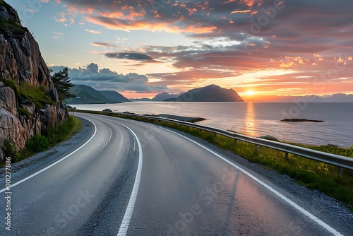 A beautiful road along the sea in Norway, with an ocean view and mountains on both sides. The sun sets behind them, casting warm hues across the sky photo