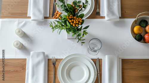 Top view of a neatly set dining table with white dishes, silverware, and a long white table runner