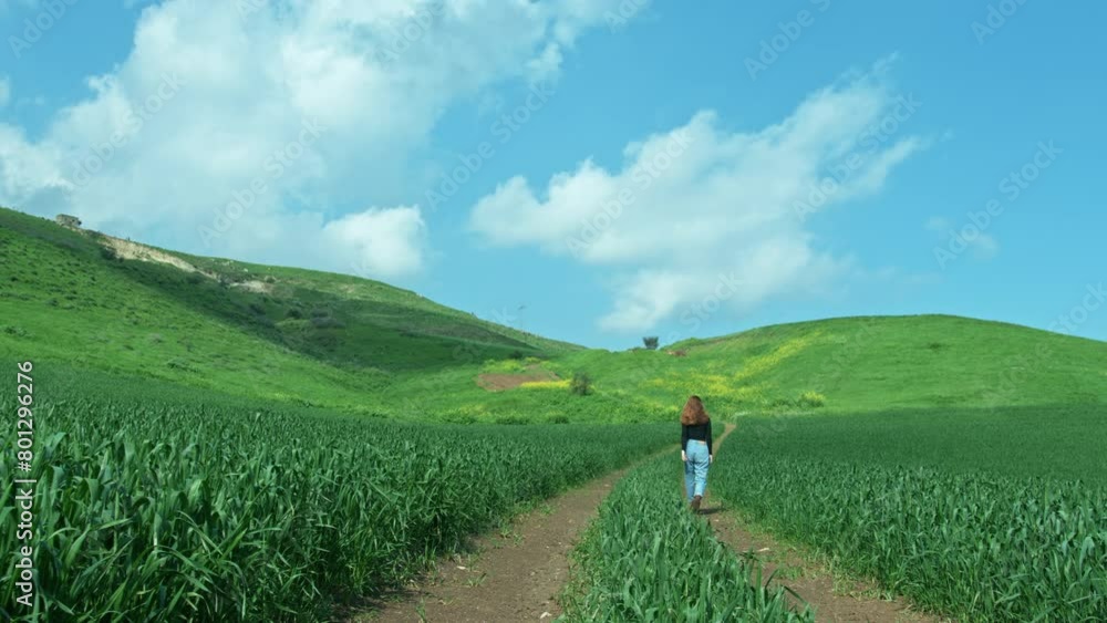 Woman walking alone along a dirt road by fields Woman walking alone along a dirt road by fields