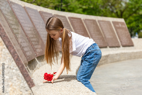 The memory of soldiers in Great Patriotic War. Little girl laying red carnations at the monument to fallen soldiers in world War II. Victory Day on May 9. photo