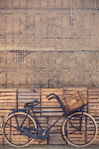 Vintage black cargo transport bicycle with crate carrier in front of old wooden crates and concrete wall