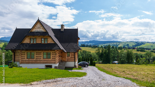 Fototapeta Naklejka Na Ścianę i Meble -  What a view the owner of this wooden house just outside Dzianisz, Poland, has: Green fields, small mountains, woods, and clouds on a blue, summer sky.