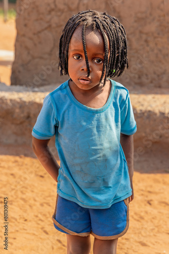 african village, small child girl with braids in front of a mud house © poco_bw