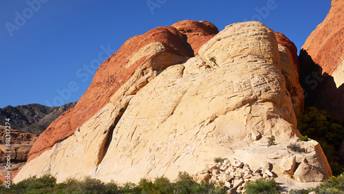 USA, Nevada, Red Rock Canyon. Eboulement de rochers depuis une montagne à la roche rouge et blanche de Red Rock Mountain dans une vallée du désert de buissons secs et de cailloux.