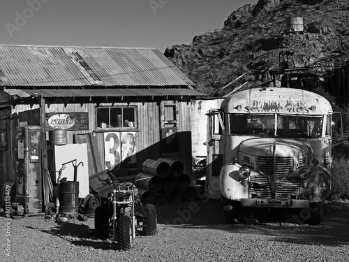 USA, Nevada. Village fantôme abandonné depuis 1940 au pied d'une montagne et sa mine, avec sa vielle station service et son épave de bus scolaire. Image noir et blanc.