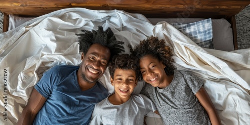 A happy mixed-race family of four in pajamas lying in a row on a bed with a blanket at home. Loveful parents of two. Beautiful girls cuddling with parents before bedtime photo