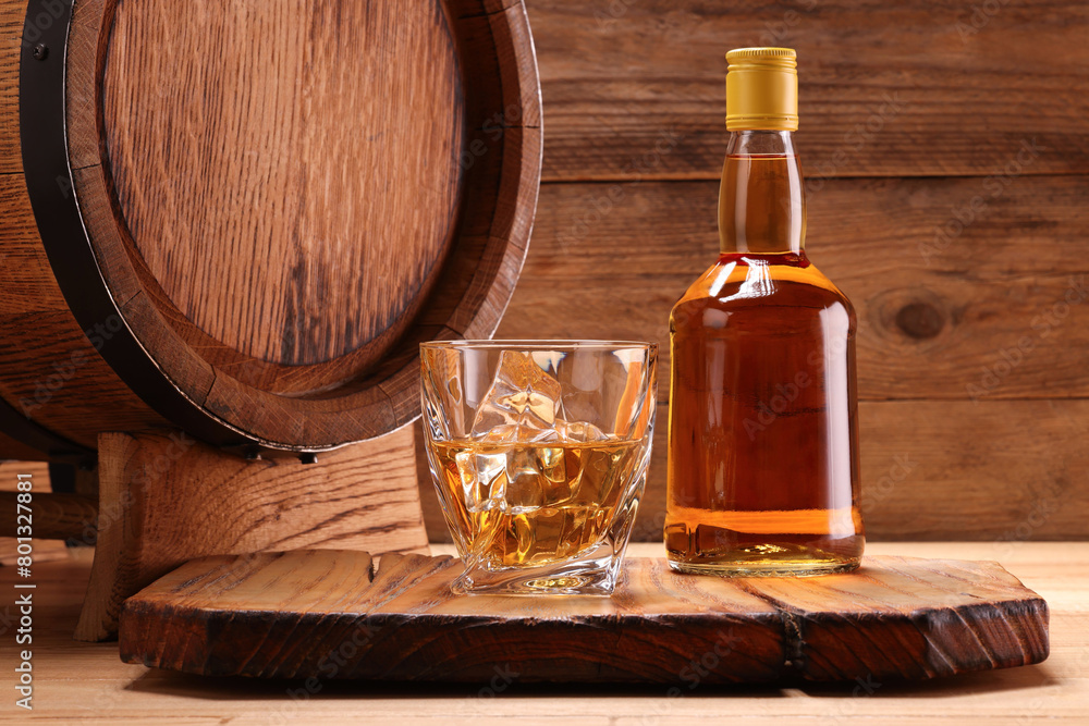 Whiskey with ice cubes in glass, bottle and barrel on wooden table Whiskey with ice cubes in glass, bottle and barrel on wooden table