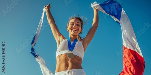 Athletic youngster cheering and clutching French flag after competition. A smiling, fit, athletic woman celebrating her Olympic gold medal. Raising national flag