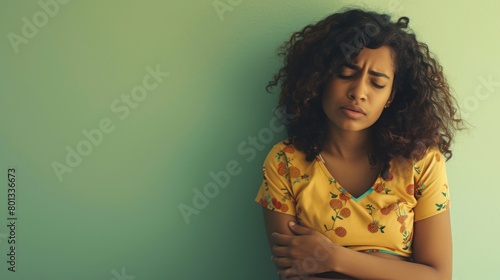 Woman sitting with a painful expression, holding her stomach, experiencing discomfort from PMS and menstrual cramps photo