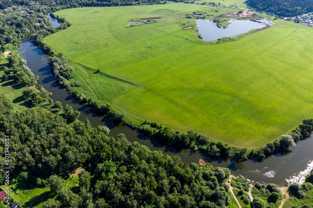 Fototapeta premium Aerial landscape with a view of a river surrounded by a green field and forest