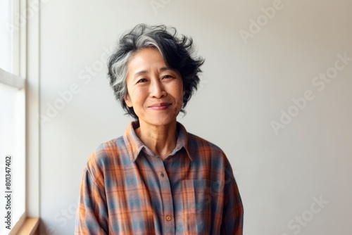 Portrait of a cheerful asian woman in her 70s wearing a comfy flannel shirt in modern minimalist interior