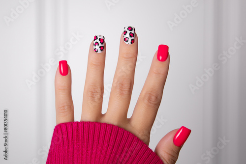 Beautiful female hand with pink manicure nails, leopard print design on white background
