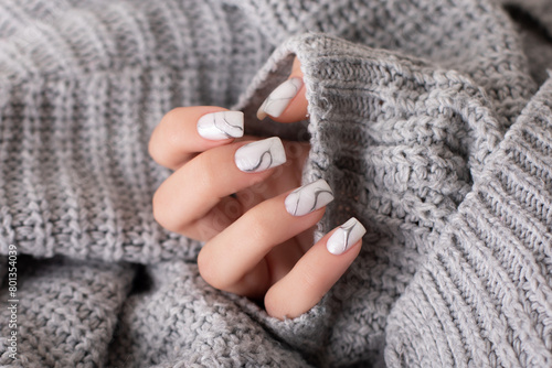 Beautiful female hand with beige and grey manicure nails on wool background
