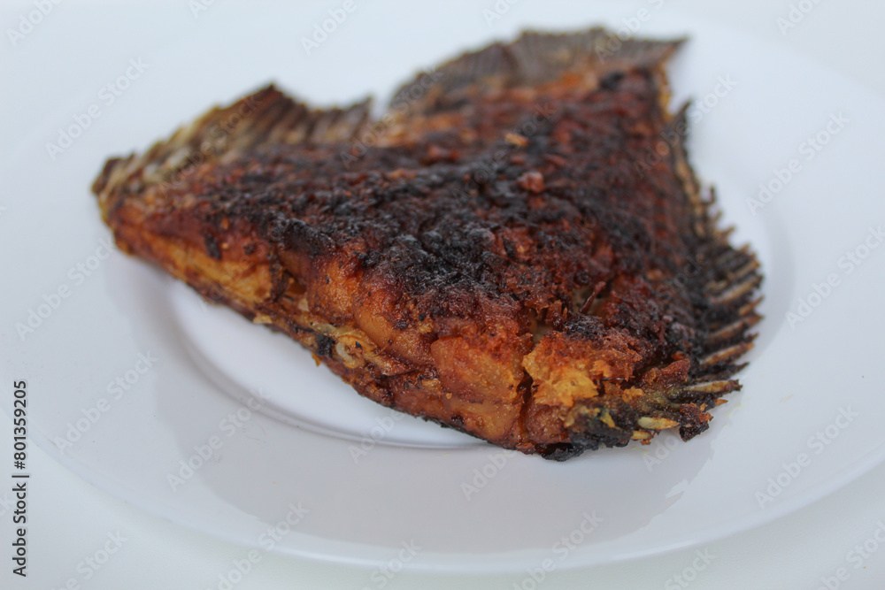 Grilled gourami fish tail, on a white plate, isolated on white background Grilled gourami fish tail, on a white plate, isolated on white background